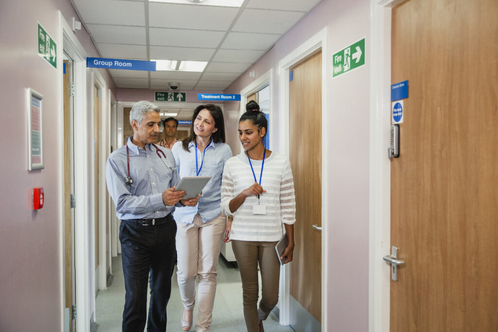 Three doctors in conversation walk down a hospital corridor