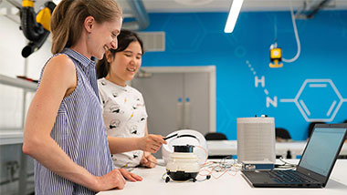 Smiling professor and student working with a computer and futuristic white device in a laboratory.