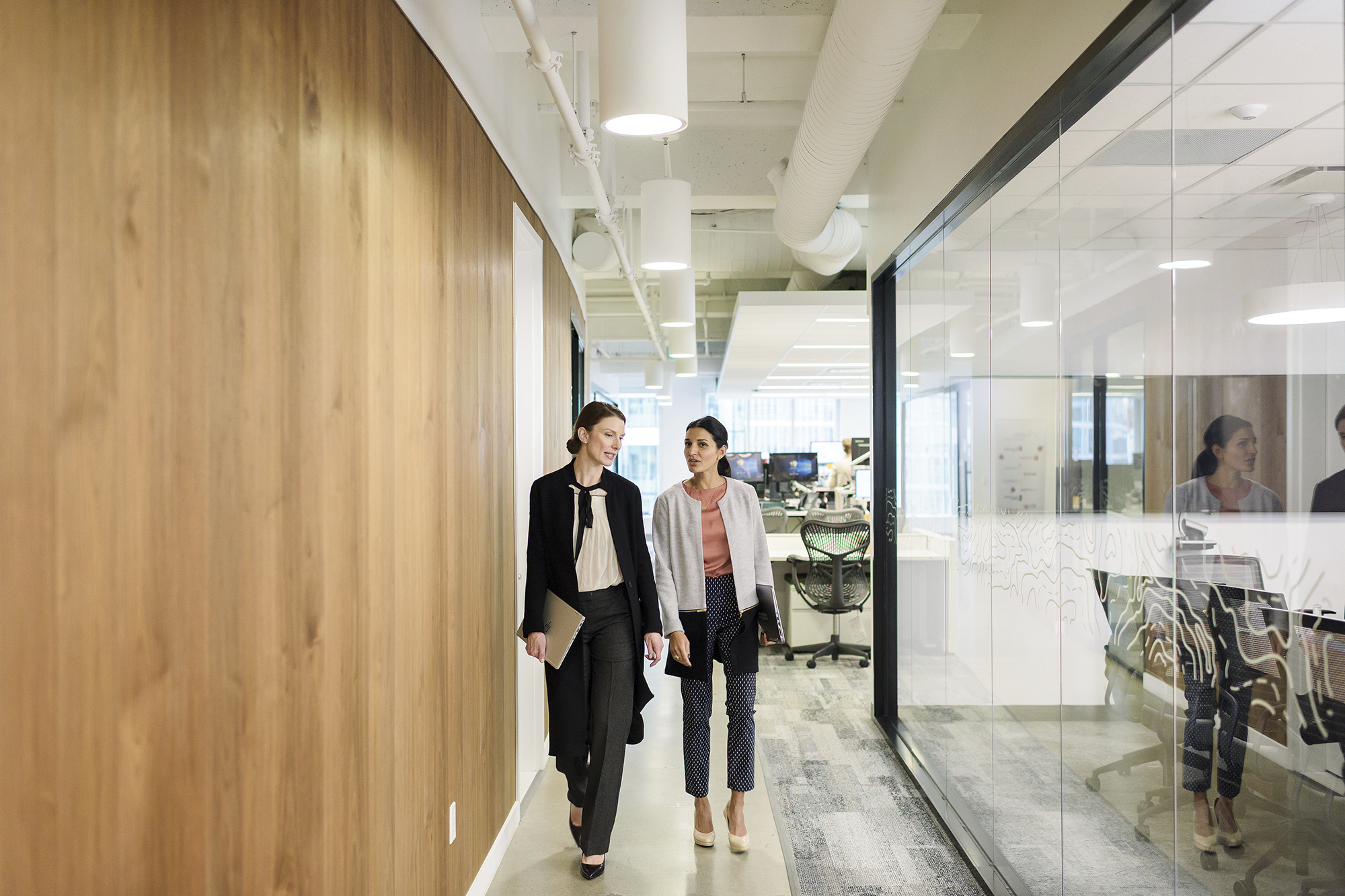 Two coworkers walking down the hallway talking.