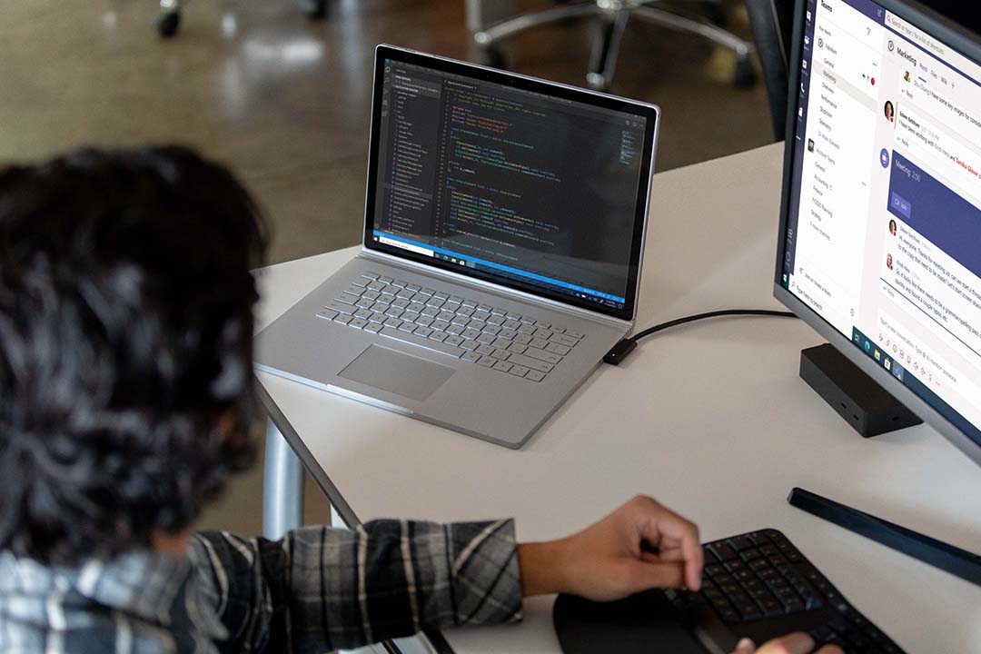 Commercial contextual lifestyle image of adult male at desk workstation on Surface Book 3 in Microsoft Azure and Microsoft Teams.