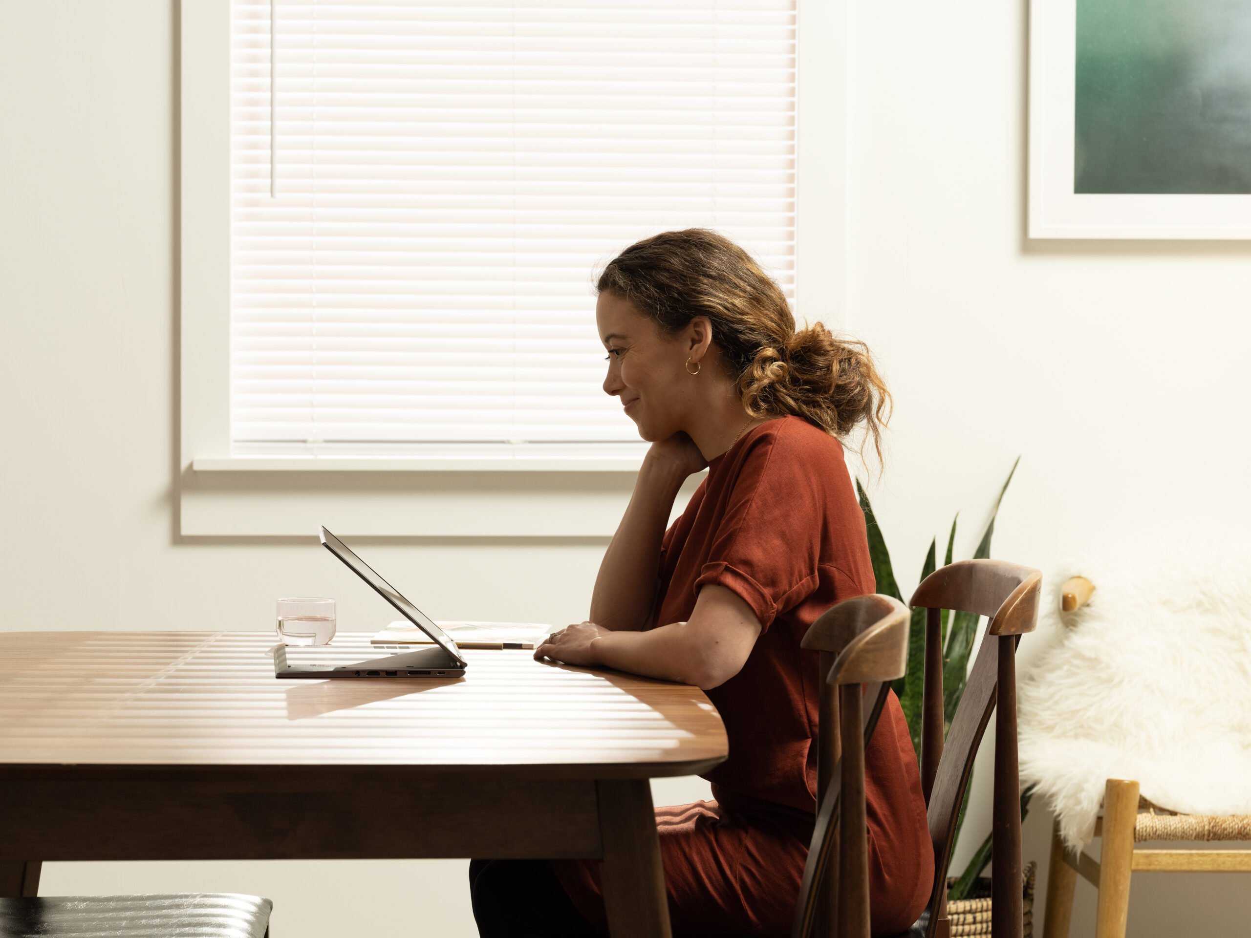 Side view of a woman working at a table on a tablet.
