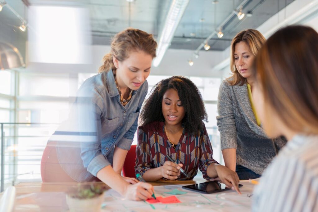Four people stand around a table while writing ideas down on sticky notes.