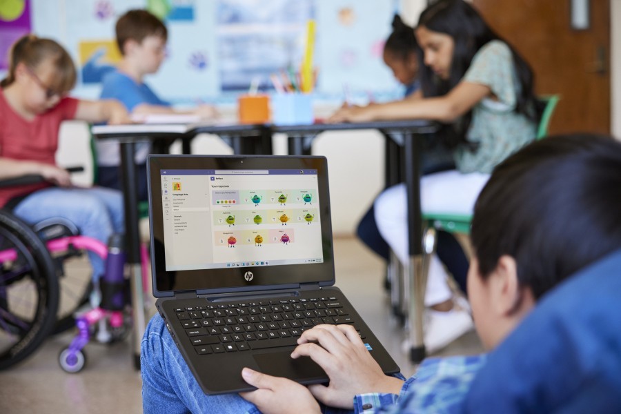 Over the shoulder perspective of a student using Reflect on a laptop with several classmates in the background.