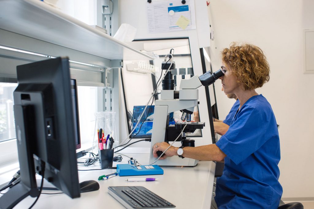 Profile of lab technician working on microscope in a bright lab