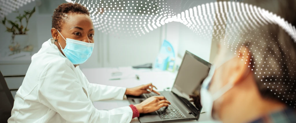 a doctor typing on a laptop and looking at a patient