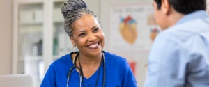 A person in scrubs smiling looking at another person.