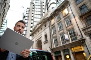 Male commuter holding Microsoft tablet (screen not shown). He is standing on city street, looking over tablet.