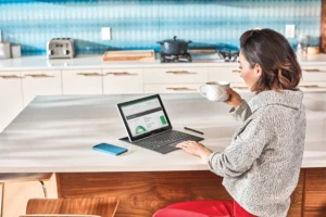 Woman interacting with Samsung GalaxyBook laptop. She is on Excel, via Winders Virtual Desktop and is drinking coffee..