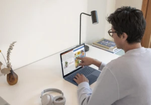 Adult male at home working on Surface laptop 4 Ice Blue and Surface Headphones with PowerPoint and OneNote snapped on screen