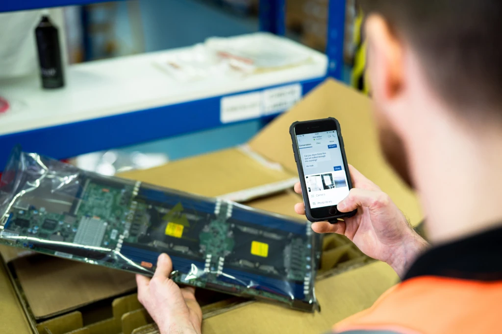 A hand holding a mobile phone. He is scanning a part into a Teams chat.