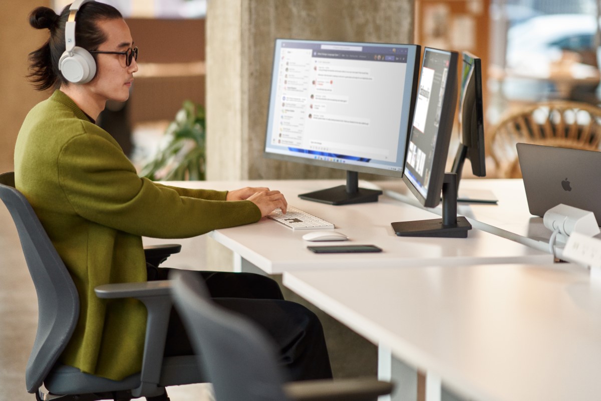 A man collaborating during a Microsoft Teams meeting while working in an open office setting on dual monitor​s.