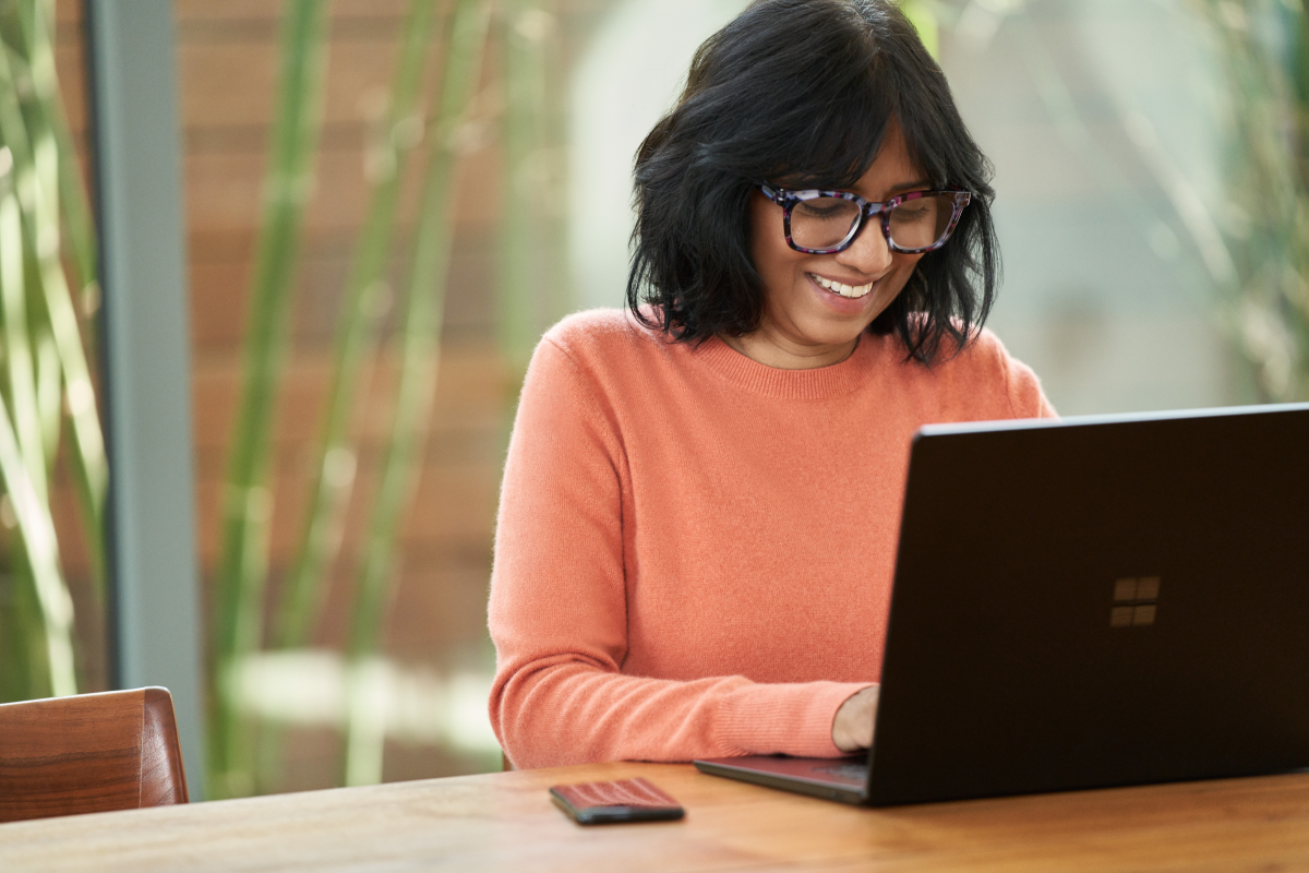 A woman who is sitting at her laptop working and smiling.