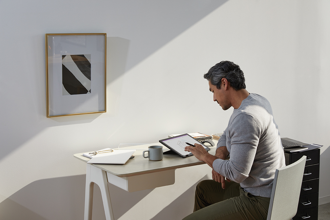 Adult male in home office environment using Microsoft OneNote at a desk with a black Microsoft Surface Pro 7 in studio mode. Black Microsoft Surface Pen in hand.