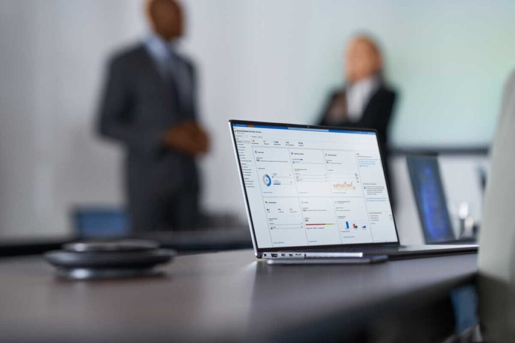 Laptop with data charts visible in foreground with out of focus people in the background.
