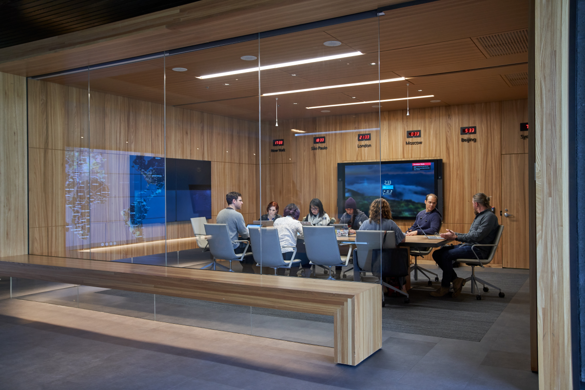Conference room or board room meeting with people sitting around table in a room with international time clocks, and a map projection.