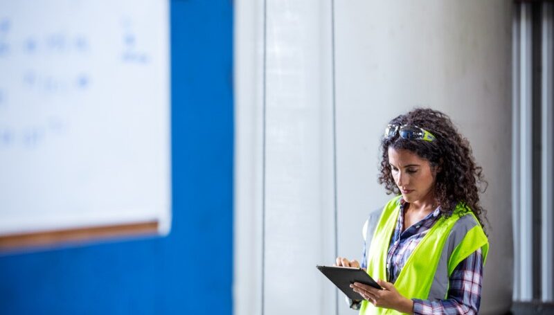 Female worker wearing neon vest and safety glasses using tablet.
