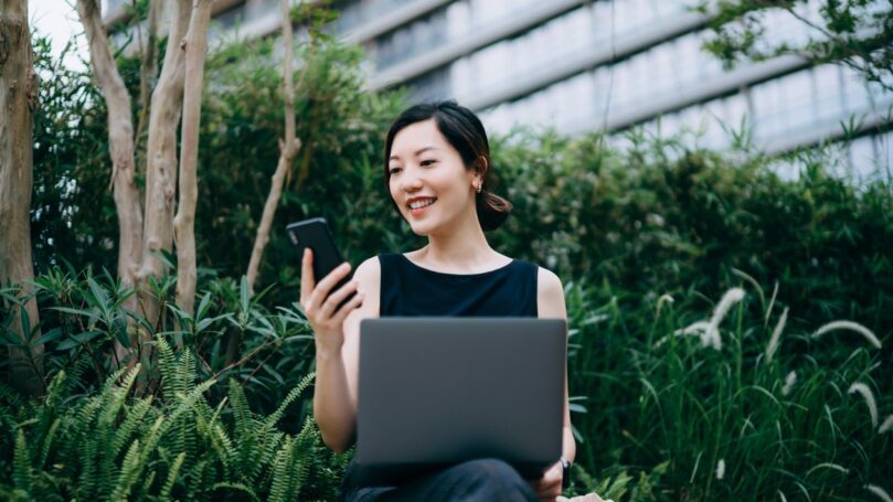 Woman working with laptop outdoors in urban office park, surrounded by green plants.
