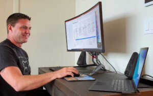 Skorupa sits at his desk and looks at his laptop. His desktop monitor displays a slide on Microsoft’s Zero Trust security model.