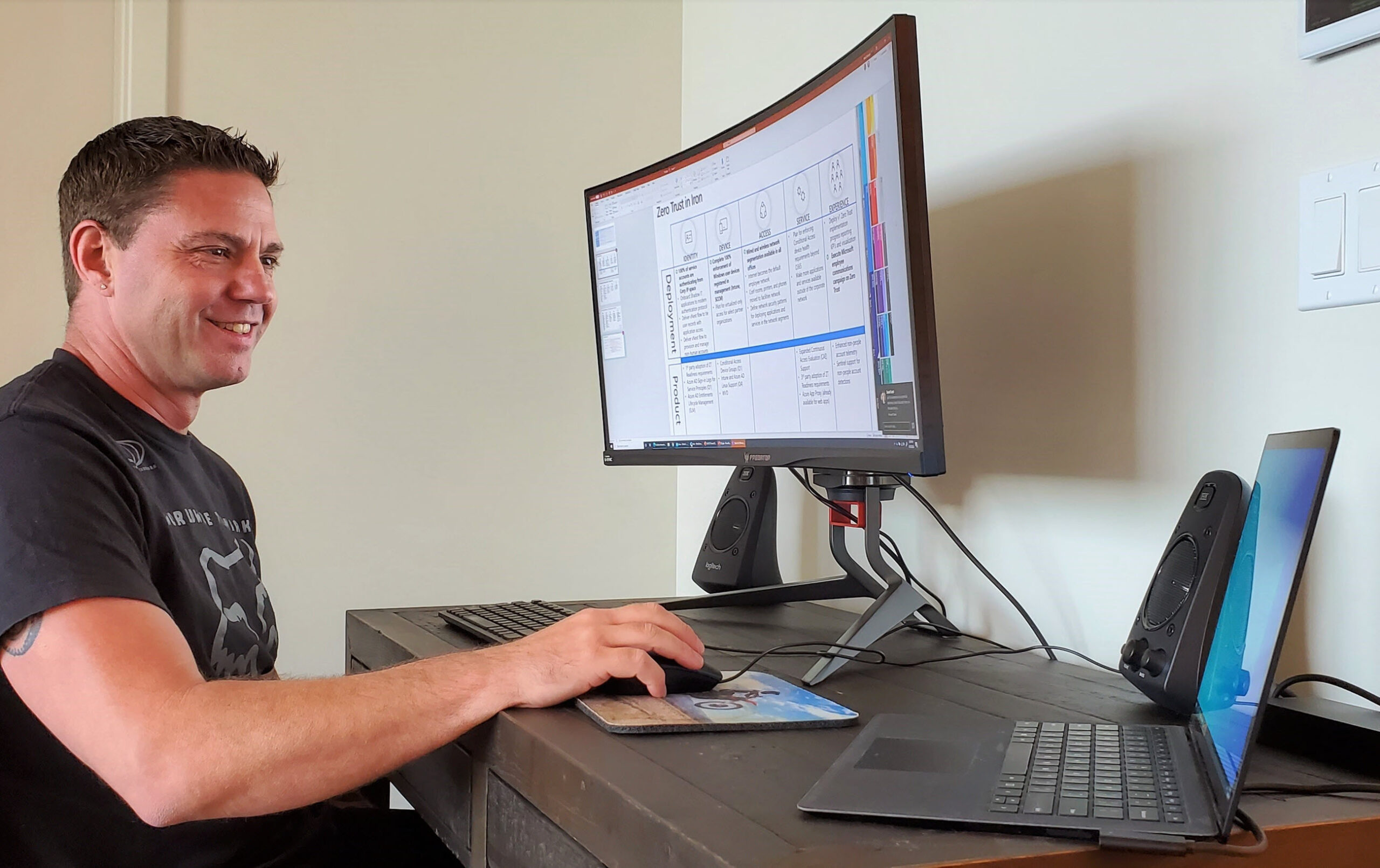 Skorupa sits at his desk and looks at his laptop. His desktop monitor displays a slide on Microsoft’s Zero Trust security model.