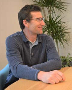 Martin sits at a desk, looking at someone he's talking to off camera.