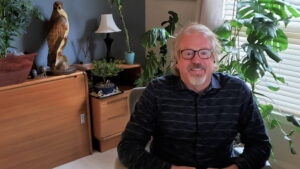 Mike Borth sits at his desk in his home office surrounded by plants.
