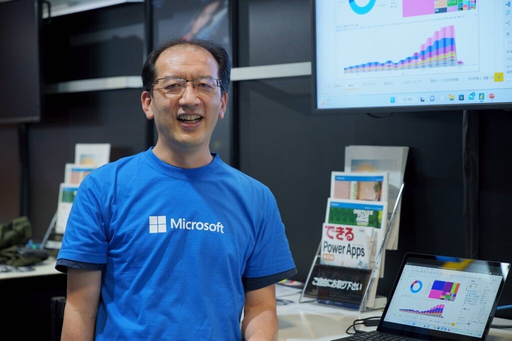 青色のマイクロソフトロゴ入りTシャツを着てカメラに向かってほほ笑む社員